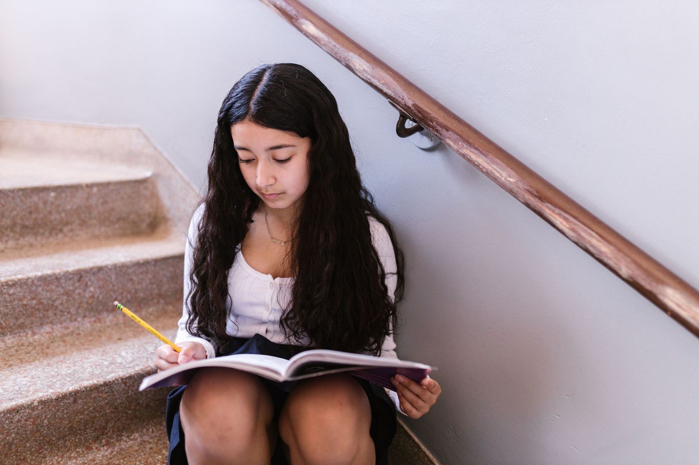 A middle school student writing in a notebook on the school stairs